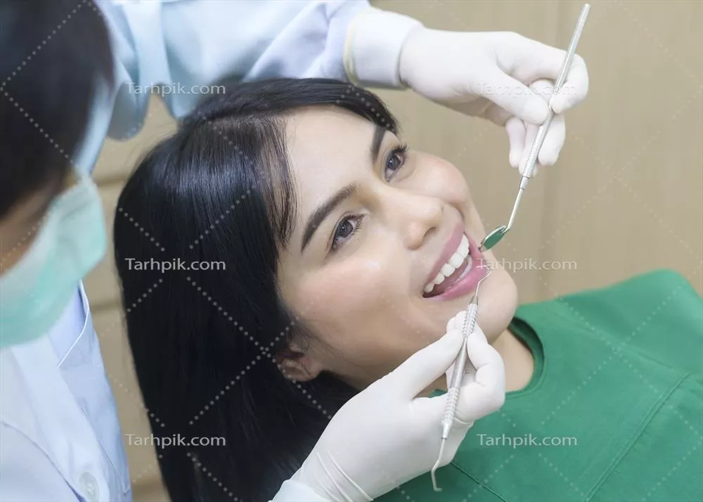 عکس معاینه دندان های یک زن جوان توسط دندانپزشک در کلینیک دندانپزشکی