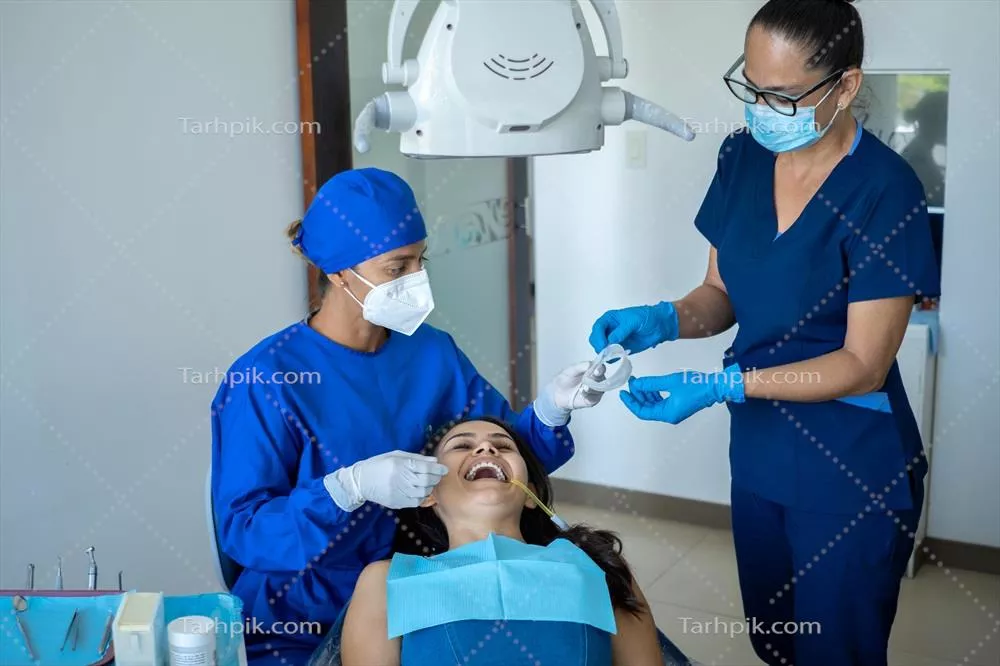 عکس دندانپزشک جوان و دستیار زن در حال معاینه بیمار