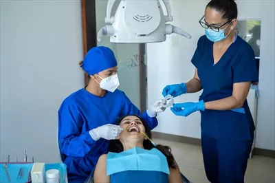 عکس دندانپزشک جوان و دستیار زن در حال معاینه بیمار