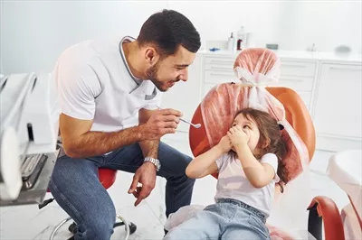 عکس دختر بچه ای که به دندانپزشک مرد در کلینیک مراجعه می کند