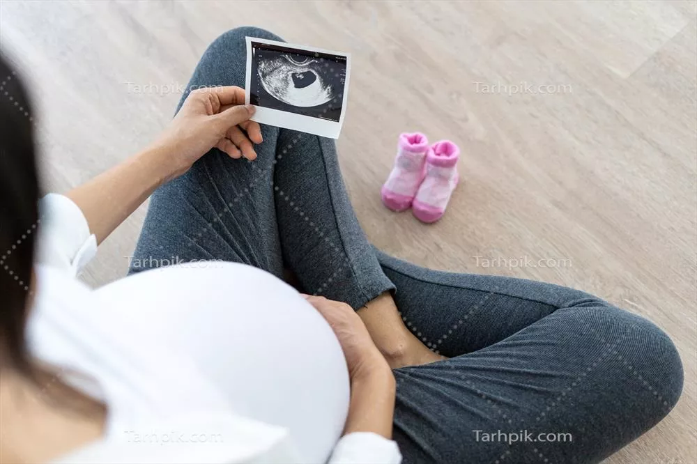عکس زنی باردار در حال مشاهده سونوگرافی جنین و لمس شکم خود