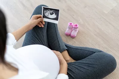 عکس زنی باردار در حال مشاهده سونوگرافی جنین و لمس شکم خود
