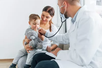 عکس پسر کوچک در حال معاینه توسط دو پزشک در کلینیک پزشکی