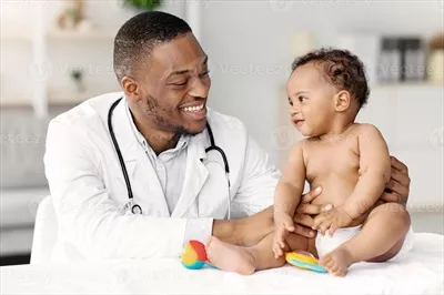 عکس تصویری از پزشک سیاه پوست در حال معاینه نوزاد پسر در مطب