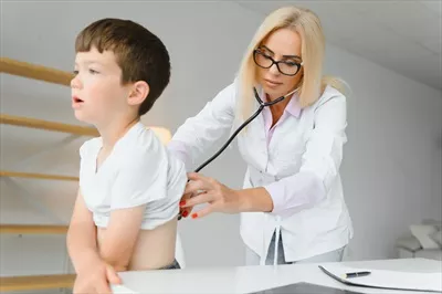 عکس پزشک اطفال در حال معاینه یک پسر بچه دوست داشتنی با گوشی پزشکی