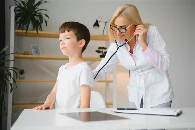 عکس پزشک اطفال در حال معاینه یک پسر بچه دوست داشتنی با گوشی پزشکی