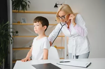 عکس پزشک اطفال در حال معاینه یک پسر بچه دوست داشتنی با گوشی پزشکی