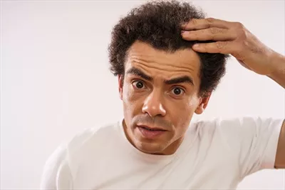 عکس مرد جوان و خوش چهره با نژاد مختلط در حال بررسی چین و چروک های پیشانی خود