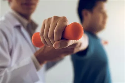 عکس فیزیوتراپیست جوان آسیایی در حال کمک به بیمار برای انجام تمرینات با وزنه