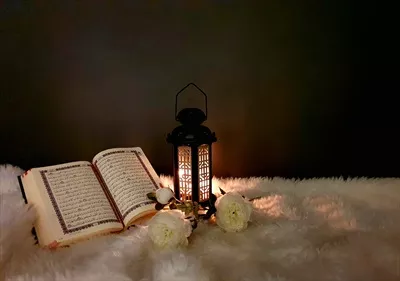عکس فانوس رمضان با رنگ مشکی و تزئینات چوبی در کنار قرآن کریم