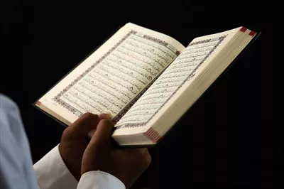 عکس مردی در حال مطالعه قرآن با دقت و تمرکز در یک محیط آرام