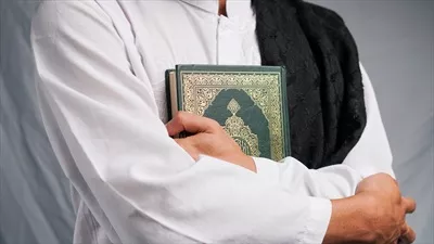 عکس مردی که با دستانش قرآن را در آغوش گرفته و تسبیحی در دست دارد
