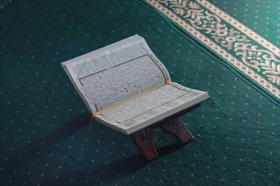 عکس تصویری نزدیک از قرآن کریم بر روی سجاده سبز در فضای اسلامی