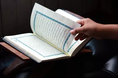 عکس تصویری نزدیک از دست که صفحه ای جدید از قرآن را ورق می زند