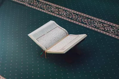 عکس تصویری نزدیک از قرآن کریم بر روی سجاده سبز رنگ با مفهوم اسلامی