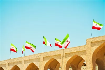 عکس پرچم های ایرانی در حال وزیدن بر بام یک ساختمان در روزی آفتابی