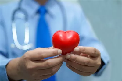 عکس پزشک در حال نگه داشتن قلب قرمز در بیمارستان به عنوان نماد عشق و مراقبت