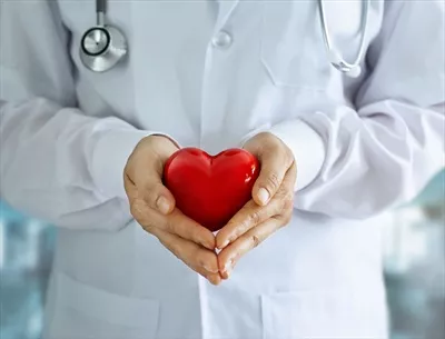 عکس تصویری از پزشک با گوشی پزشکی و قلب قرمز در دستانش در بیمارستان