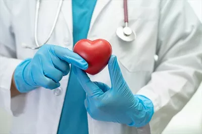 عکس پزشک در حال نگه داشتن قلب قرمز در بخش بیمارستان برای ترویج سلامت