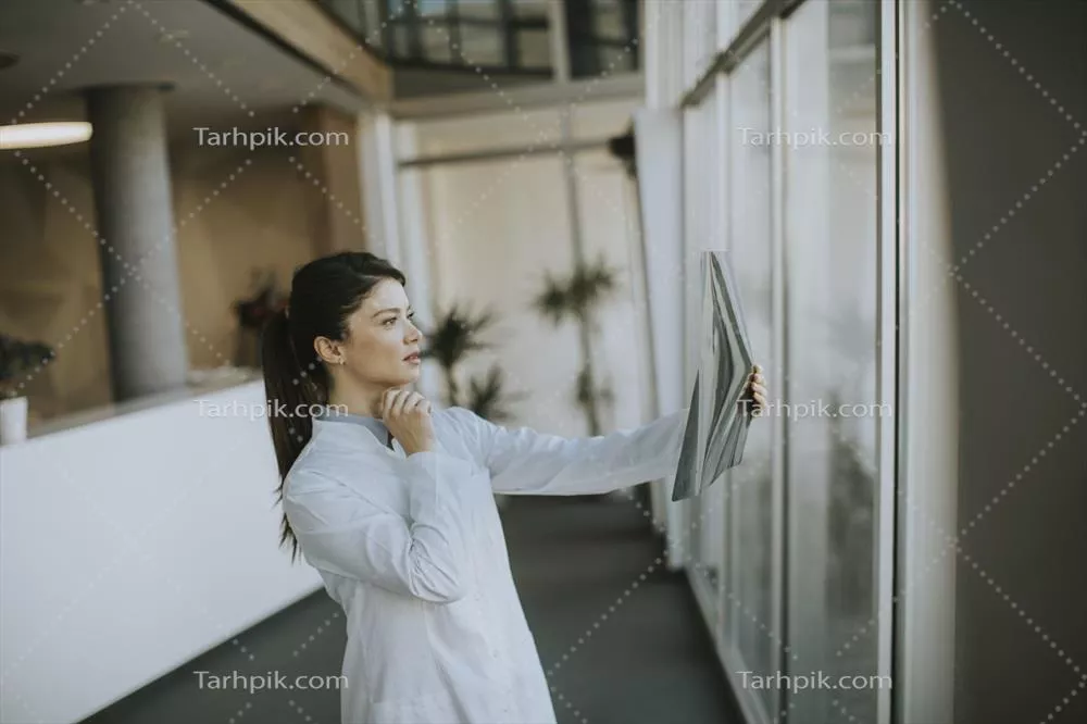 عکس پزشک جوان زن در حال بررسی تصویر اشعه ایکس در مطب پزشکی