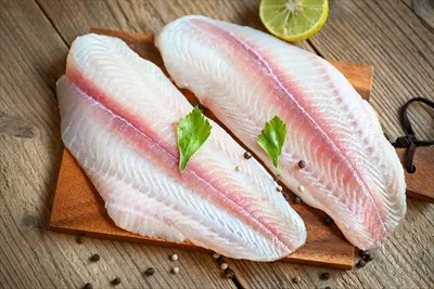 عکس فیله ماهی پنگاسیوس تازه بر روی تخته چوبی با ادویه جات و لیمو