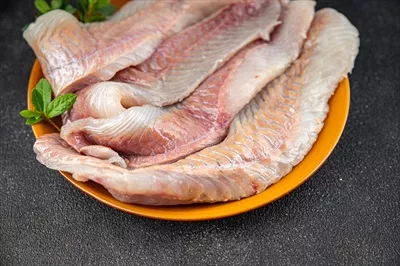 عکس فیله ماهی تازه و خام از نوع کاد یا هالیبوت بر روی میز با فضای خالی