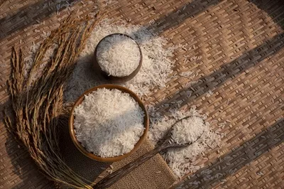 عکس نور و سایه بر روی سطح برنج سفید در کاسه سرامیکی با قاشق چوبی