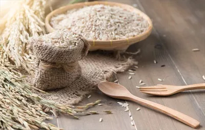 عکس برنج قهوه ای یاسمنی در سبد بامبو بر روی پس زمینه چوبی تیره