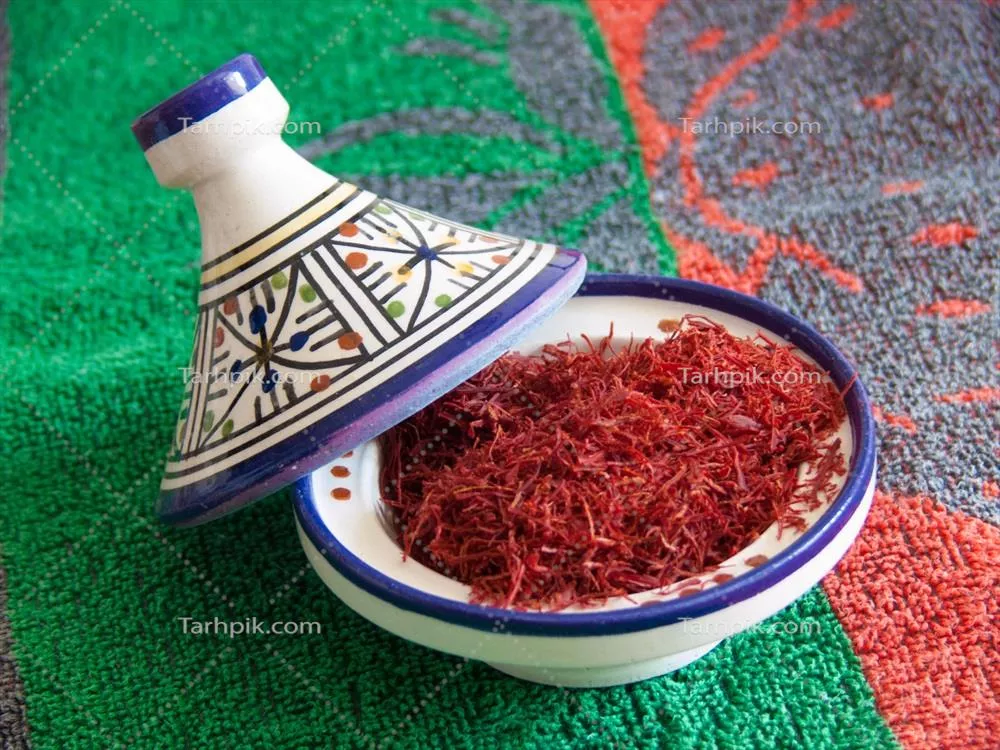 عکس کاسه ای پر از زعفران قرمز بر روی سفره ای سبز و آبی