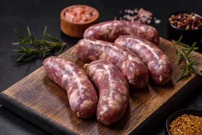 عکس سوسیس های خام گوشت خوک کبابی با ادویه و سبزیجات روی میز بتنی تیره
