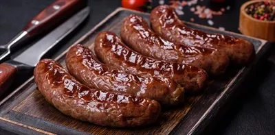 عکس سوسیس کبابی خوشمزه با مواد اولیه روی تخته برش در پس زمینه سنگی