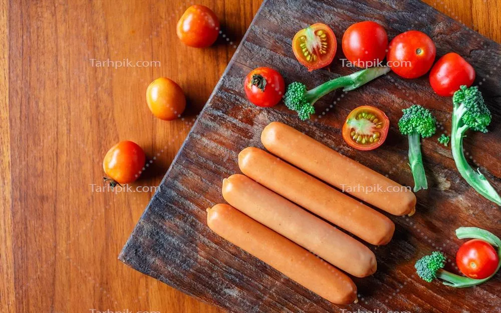 عکس سوسیس خام روی تخته چوبی همراه با بروکلی و گوجه فرنگی