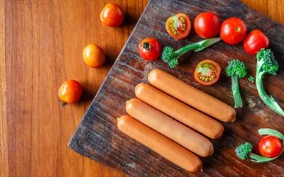 عکس سوسیس خام روی تخته چوبی همراه با بروکلی و گوجه فرنگی