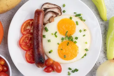 عکس یک صبحانه خوشمزه شامل تخم مرغ سرخ شده، گوجه فرنگی و سوسیس چینی