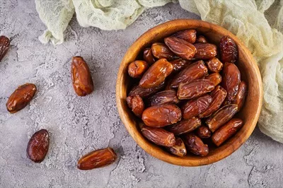 عکس میوه های خوشمزه و مغذی خرما در کاسه ای چوبی بر روی میز