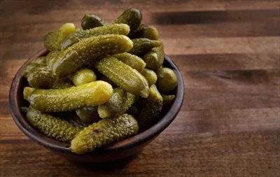 عکس یک فنجان خیارشور ترد و خوشمزه بر روی تخته چوبی قرار دارد