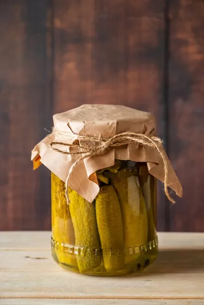 عکس خیار شور خانگی در شیشه شفاف بر روی پس زمینه چوبی با سبک روستایی