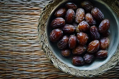 عکس کاسه ای پر از خرما بر روی میزی بافته شده و زیبا