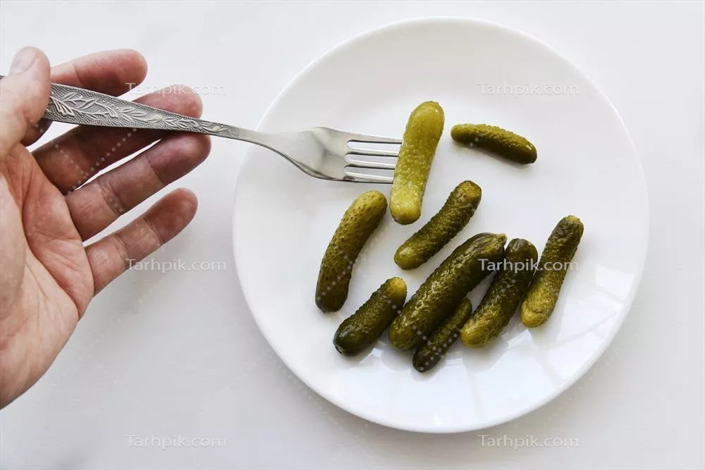 عکس ترکیب خوشمزه خیارشور سبز روی یک بشقاب سفید با چنگال