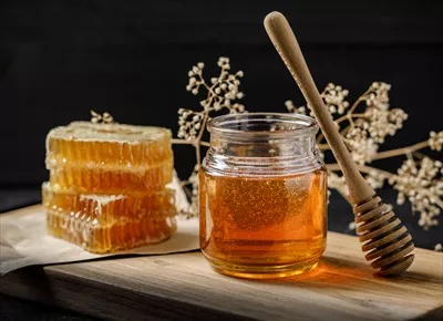 عکس عسل طبیعی و دمنوش گیاهی در کنار کندوی عسل بر روی پس زمینه سیاه