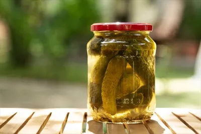 عکس خیار شور نمکی در شیشه ای روی میز چوبی در باغ با پس زمینه ای از حفظ و نگهداری