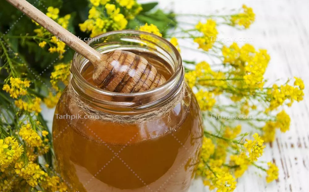 عکس شیشه عسل طبیعی در کنار گل های کلزا بر روی پس زمینه چوبی