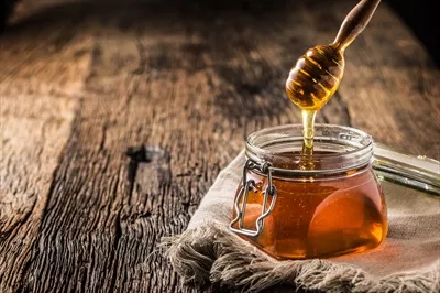 عکس زیبای یک شیشه عسل با قاشق چوبی بر روی میز چوبی قدیمی