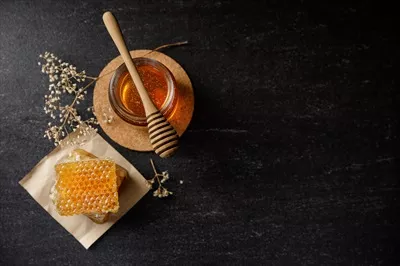 عکس عسل طبیعی و موم زنبور عسل با گل های خشک در پس زمینه سیاه