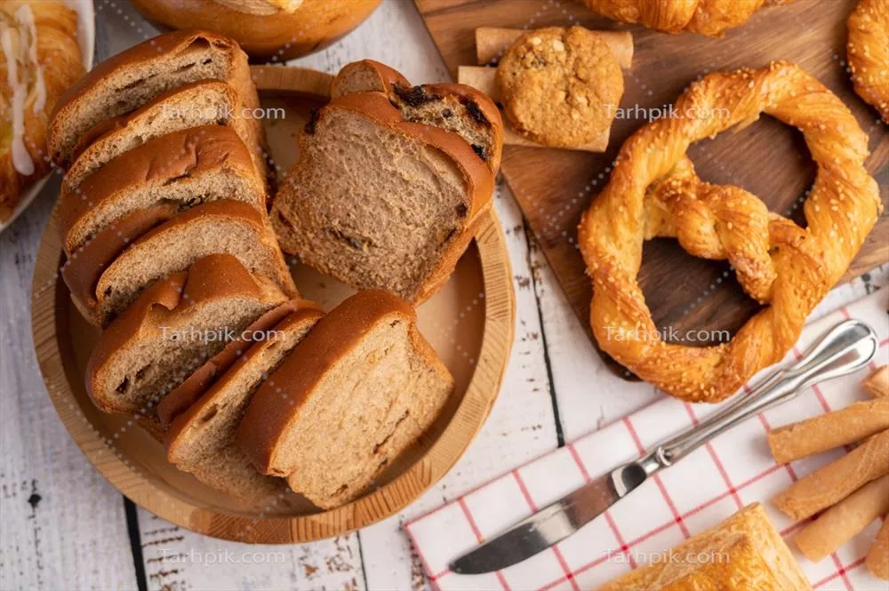 عکس برش های نان تازه در یک بشقاب چوبی روی میز چوبی سفید