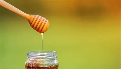 عکس عسل در حال چکیدن از قاشق چوبی بر روی پس زمینه طبیعی و زیبا