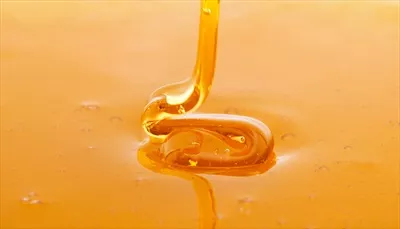 عکسی زیبا از عسل تازه و غلیظ که به آرامی در حال چکیدن است