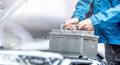عکس تعمیرکار خودرو در حال تعویض باتری معیوب خودرو در شرایط زمستانی