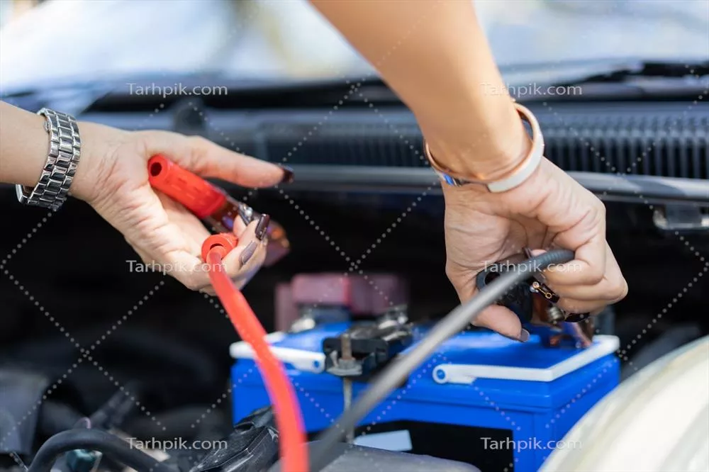 عکس نزدیک نمایی از مکانیک خودرو در حال کار بر روی باتری و کابل های الکتریکی