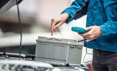 عکس بررسی عمر باتری خودرو توسط تکنسین در تعمیرگاه با استفاده از مولتی متر